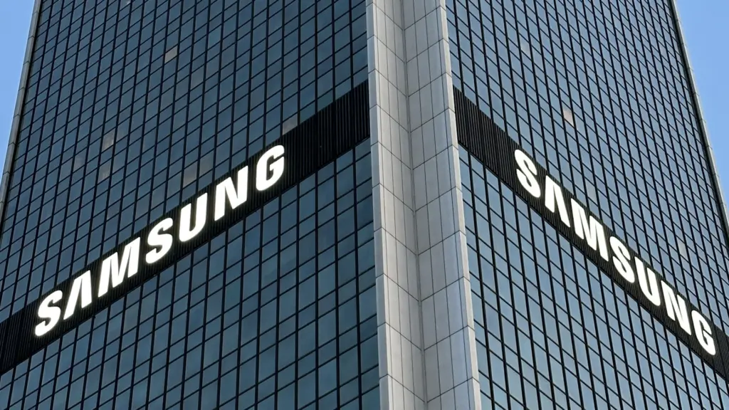 Corner of a glass office tower with large white SAMSUNG logos on two sides seeing the building at an angle.