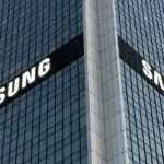 Corner of a glass office tower with large white SAMSUNG logos on two sides seeing the building at an angle.