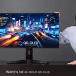Woman posing with a large gaming monitor showing a neon-race car game on a desk. The display reads QD-OLED and 4K 360Hz markers are visible.