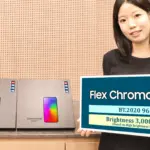 Woman standing behind a counter, holding a large sign that reads 'Flex Chroma Pixel' while two boxed devices sit on the counter beside her.