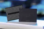 Two computer chips standing upright on a blue surface: a dense ball-grid array (BGA) chip and a dark square processor beside it.