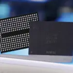 Two computer chips standing upright on a blue surface: a dense ball-grid array (BGA) chip and a dark square processor beside it.